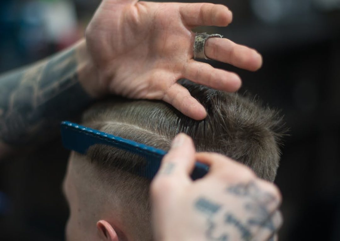 Close-up of a tattooed barber giving a stylish haircut indoors, highlighting modern grooming techniques.