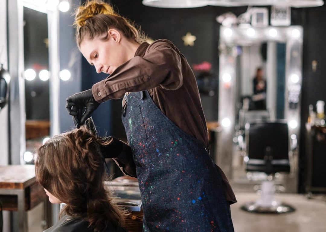 A female stylist expertly applying hair color to a client in a modern salon setting.